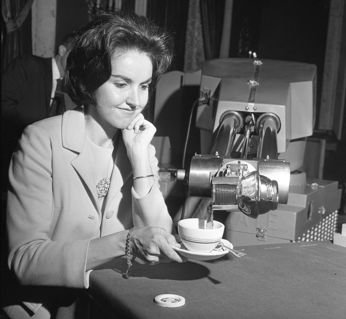 En Unimate-robotarm häller kaffe i en kopp som en kvinna håller fram