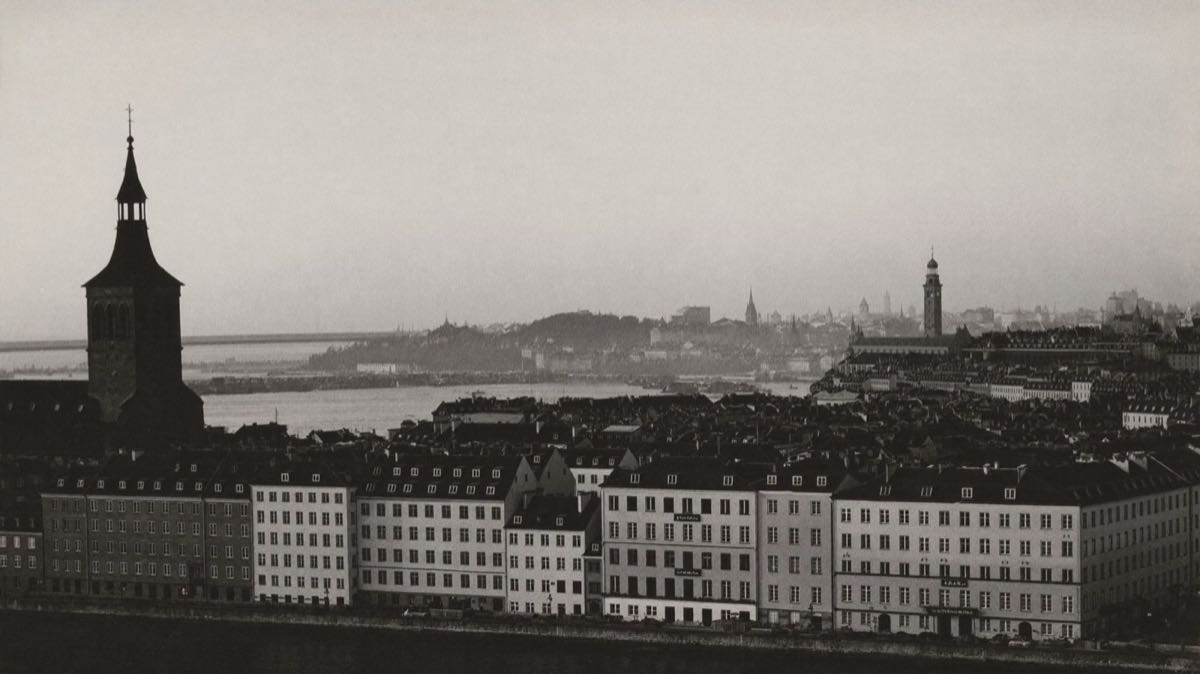 Stadssiluett vid vatten i gryningsdis, svartvitt